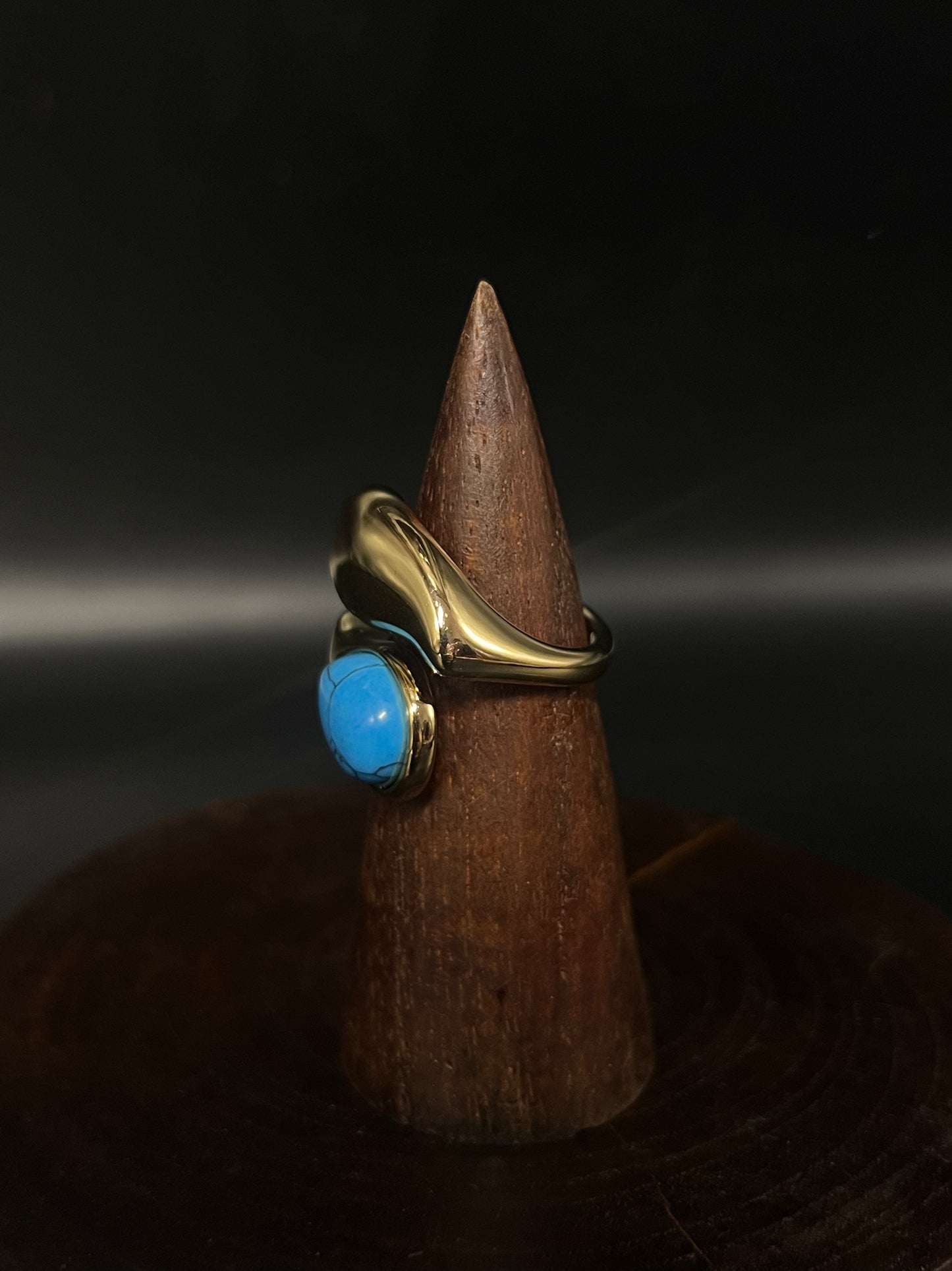 Gold ring with a blue stone on a wooden cone against a dark background